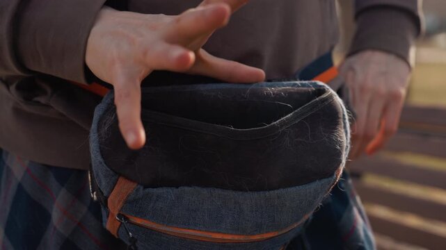 Person wearing brown sweatshirt and plaid pants adjusts straps of small blue denim bag with orange accents around their waist. focus remains on hands interacting with or inspecting empty