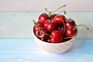 organic Red Cherries in a Bowl on a Light Blue Wooden Surface, copy space © Irina