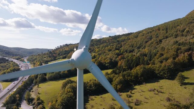 Wind turbines turn in a rural area with green fields and mountains in the background. Clean energy generation is happening here.