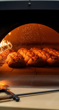 Artisan bread loaves baking inside a traditional wood fired stone oven with open flames