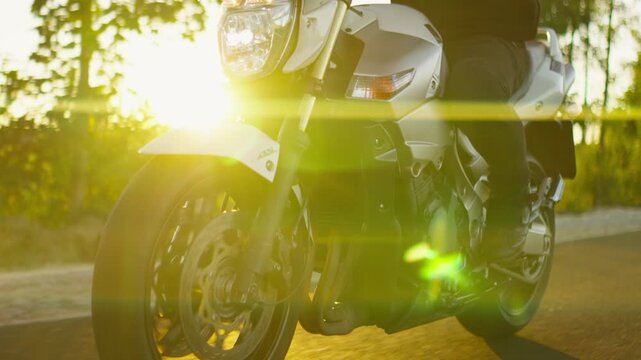 Motorcyclist riding powerful sport bike along forest road at golden sunset, capturing motion, speed, and freedom on an empty scenic countryside highway