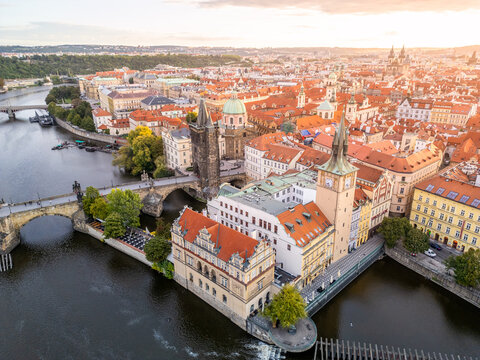 Aerial view of Charles Bridge spanning the Vltava River with historic Old Town architecture and terracotta rooftops under warm sunset light in Prague, Prague, Czechia.