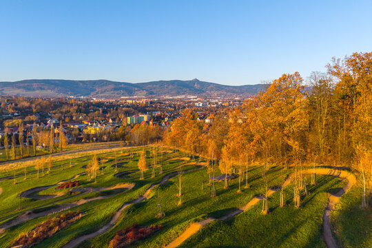 Aerial view of Vapark featuring a winding pump track set in a grassy landscape with autumn trees, overlooking the city and mountains in Liberec 30, Liberec Region, Czechia.