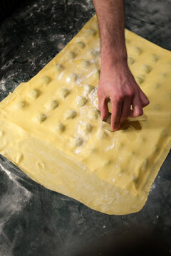 Chef Hand Cutting Fresh Homemade Ravioli Pasta with Metal Cutter