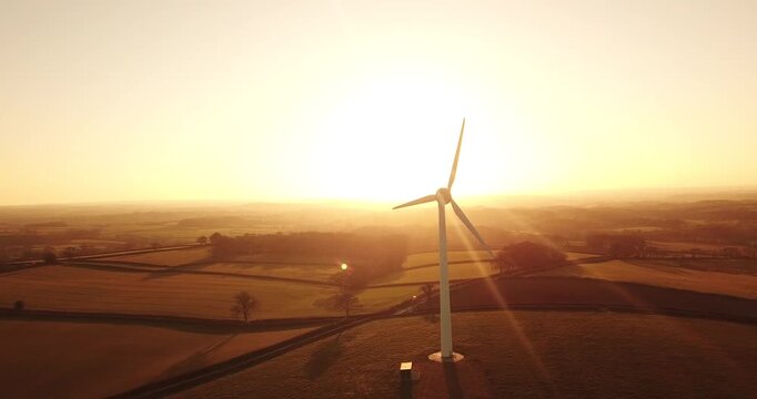 Devon, United Kingdom - 03 September 2026: Aerial view of a wind turbine standing in a rural landscape during golden hour.