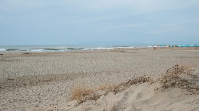 Narbonne Plage in the morning. Sea waves crashing onto the long sandy beach. Sun umbrellas in sand-and-sky colors. Mediterranean natural coastal aesthetic. Minimal. Copy space.