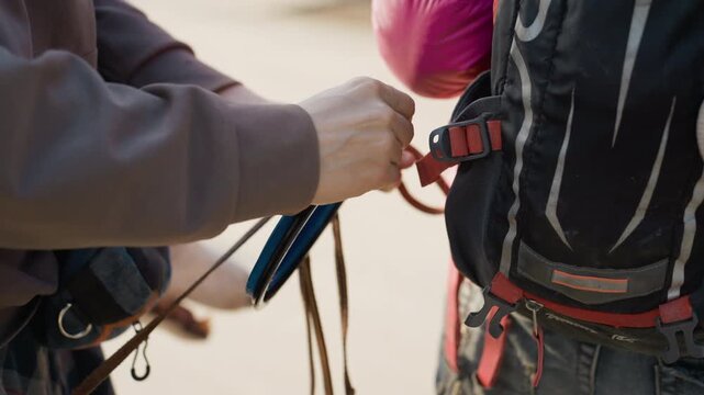 Person attaches blue climbing quickdraw to another person harness focusing on hands and gear. interaction involves securing carabiners onto red straps of outdoor safety equipment in active