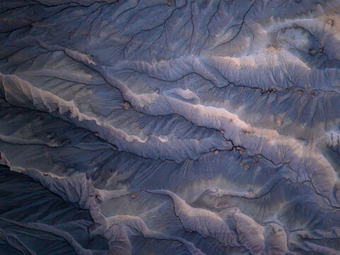 Aerial view of the rugged, eroded desert landscape near Hanksville, featuring intricate drainage patterns, deep gullies, and textured rock formations in Hanksville, Utah, United States.