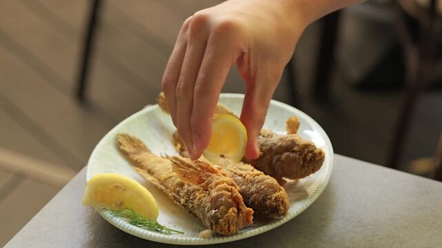 Hand squeezing lemon juice over fried goby fish