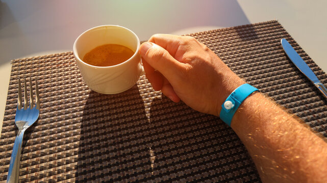 Male hand wearing colorful hotel wristband holding warm coffee mug vacation resort morning lifestyle concept, travel holiday relaxation.