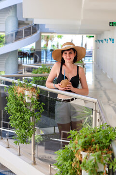 Woman in hat standing in hotel holding coconut with straw, tropical vacation drink, resort lifestyle, summer holiday concept.
