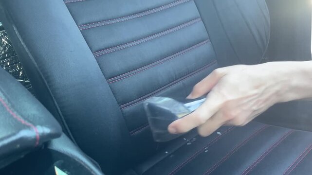 Car seat detailing process using extractor vacuum nozzle to clean black upholstery with red stitching in professional auto maintenance workshop. High quality 4k footage