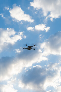 Quadcopter drone flying in the blue sky surrounded by white clouds