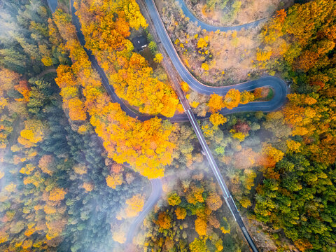 Aerial view of the autumn railroad viaduct surrounded by vibrant yellow and orange forest foliage with winding tracks and light mist in Mikulov, Usti nad Labem Region, Czechia.