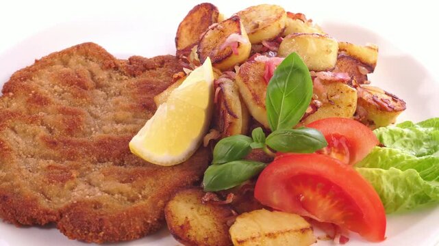 Wiener Schnitzel paniert auf einem Teller mit Bratkartoffel auf wei&szlig;em Hintergrund - Drehteller