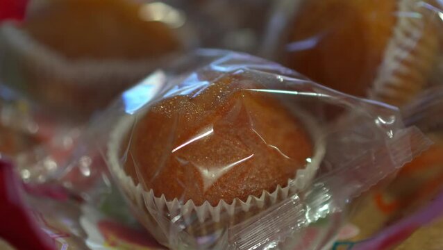 A close-up shot looking inside an open plastic bag filled with individually wrapped mini muffins or cupcakes on a wooden surface.