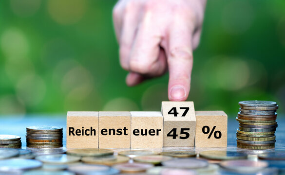 W&uuml;rfel mit &bdquo;Reichensteuer 45 auf 47 %&ldquo; und M&uuml;nzen als Symbol f&uuml;r Steuererh&ouml;hung, Umverteilung und deutsche Finanzpolitik.