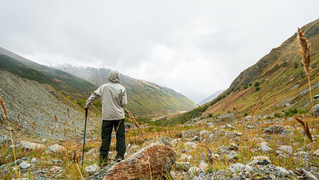 Hiker standing with trekking pole looking at autumn mountain valley near Shkhara glacier in Georgia.