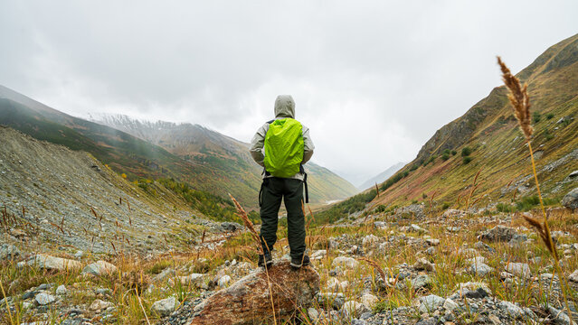 Hiker with green backpack standing on rock looking at autumn mountain valley near Shkhara glacier in Georgia.