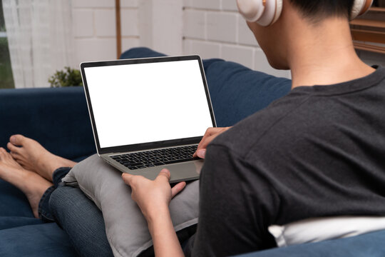 Young man typing on a laptop while wearing headphones at home, representing remote work, productivity, technology, and a comfortable digital lifestyle