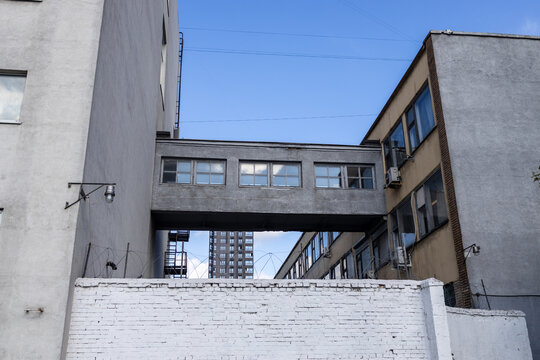 Concrete skywalk bridge connecting two urban industrial buildings behind white brick wall