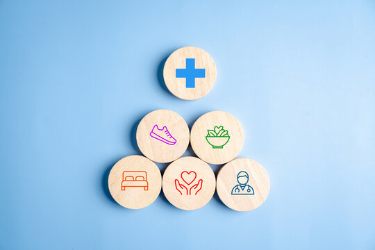 Health and wellness lifestyle concept. Wooden block pyramid with medical cross exercise diet sleep and care icons on blue background.