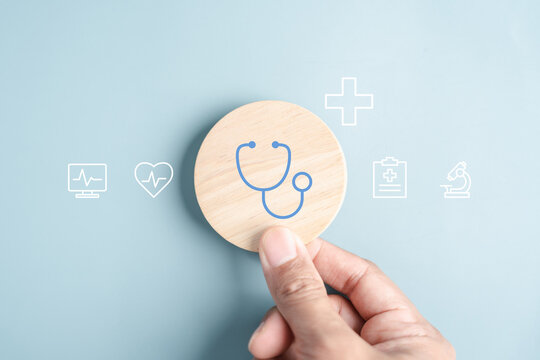 Medical healthcare and wellness prevention concept. Hand holding wooden block with stethoscope and health checkup icons.