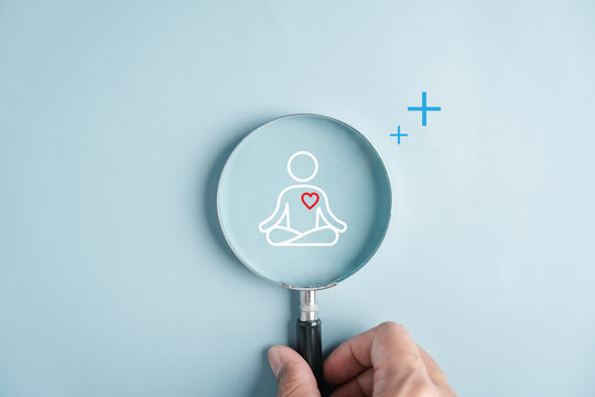 Mental health wellness lifestyle and mindfulness meditation concept. Hand holding magnifying glass focusing on lotus pose and heart icon.