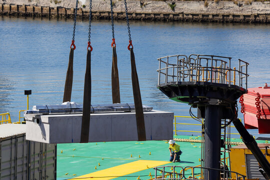 View of a heavy lift operation with a suspended precast concrete block being moved by crane rigging, with a construction worker kneeling on the deck in Rozelle, New South Wales, Australia.