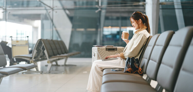 Young adult asian woman tourist to transit using wifi laptop freelancer remote work at waiting area international airport terminal for departure