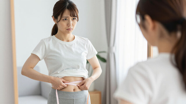 Japanese Young Woman Measuring His Waist After Touching Belly Fat, Weight Management and Health Concern Concept, Copy space on the left