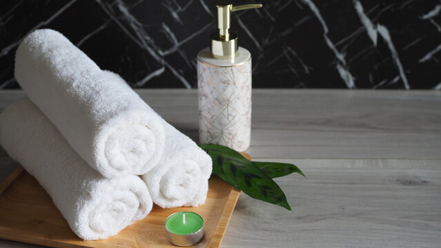 Luxury spa wellness still life with rolled white towels, elegant soap dispenser and green candle on a wooden tray against a dark marble background, creating a calm relaxation atmosphere.