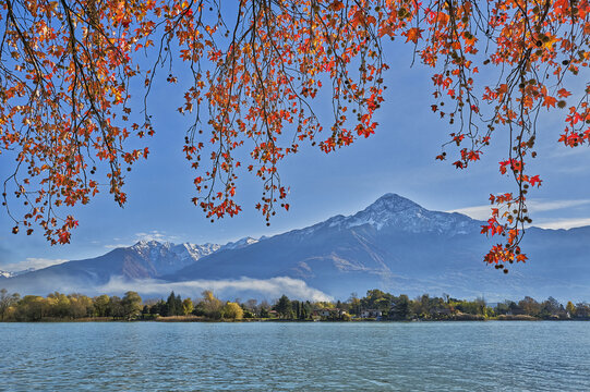 View of the autumn foliage framing the serene waters of Lake Como with the snow-dusted mountains in the background in Gera Lario, Lombardia, Italy.