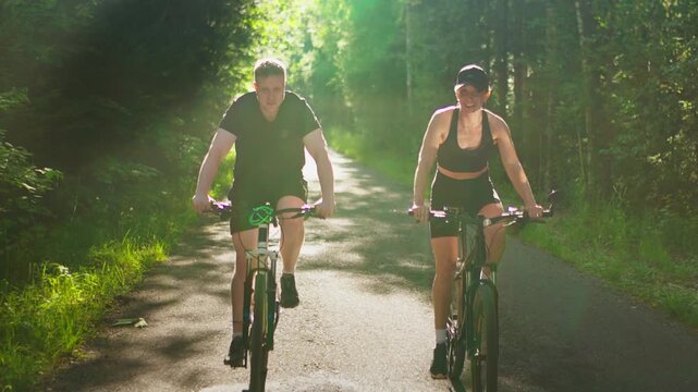 Active couple cycling together on a sunny forest path, enjoying outdoor fitness, healthy lifestyle, and nature during a bright summer day ride