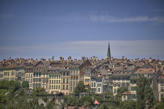 View of the historic old town of Bern with its characteristic terracotta rooftops, stone buildings, and a church spire under a clear blue sky in Bern, Canton of Bern, Switzerland.