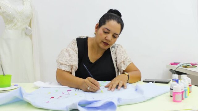 A Colombian fashion designer is painting a garment with special tempera paints on a table inside a sewing workshop in Neiva, Huila, Colombia. Concept of handmade, textile industry and hobbies