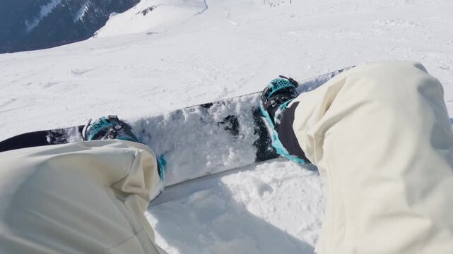 Snowboarder strapping into bindings before descending a steep snowy mountain slope with panoramic alpine views and untouched powder on a clear winter day