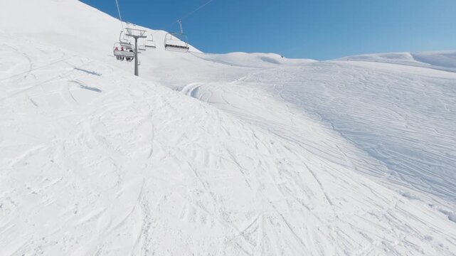 Snowy mountain ski slope with chairlift gliding above freshly groomed powder and scattered tracks under clear blue winter sky on bright sunny day