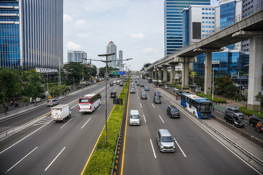 View of a busy multi-lane highway with cars, buses, and an elevated rail track, surrounded by modern office buildings in Jakarta, Jakarta, Indonesia.