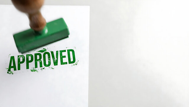 Green rubber stamp stamping the word approved on white paper document with copy space