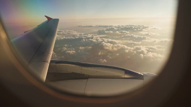 Scenic Airplane Window View of Wing Floating Above Clouds Illuminated by Sunset. Airplane Wing Flying Above Low Clouds with Dramatic Sunset Light in the Sky
