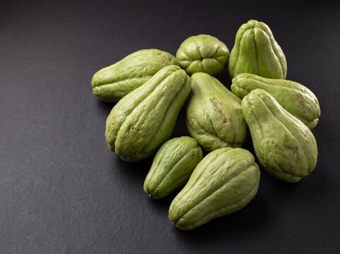 Fresh labu siam chayote squash cluster with wrinkled ridged skin on dark background