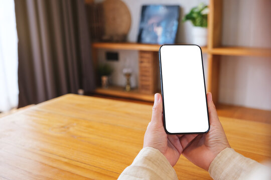Mockup image of a woman holding and using mobile phone with blank desktop white screen at home