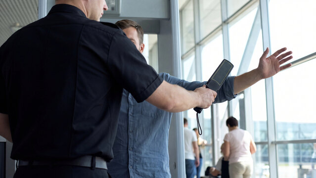 A TSA security officer uses a handheld metal detector wand to screen a passenger at an airport checkpoint. Concept of aviation security and law enforcement screening protocol.
