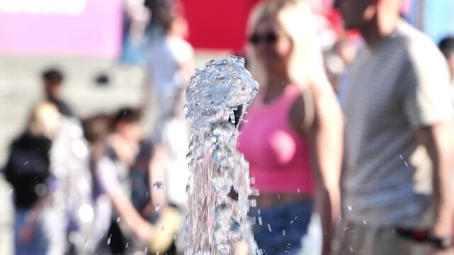 Refreshing water jet splashing in a city fountain with blurred crowd on a sunny summer day