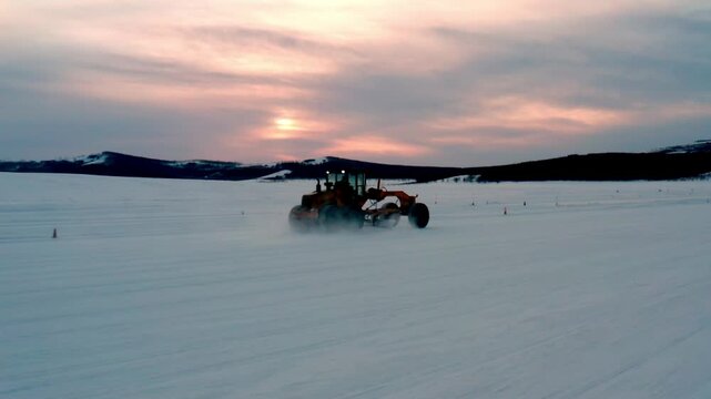 Motor Grader Driving Across a Frozen Plain at Dusk