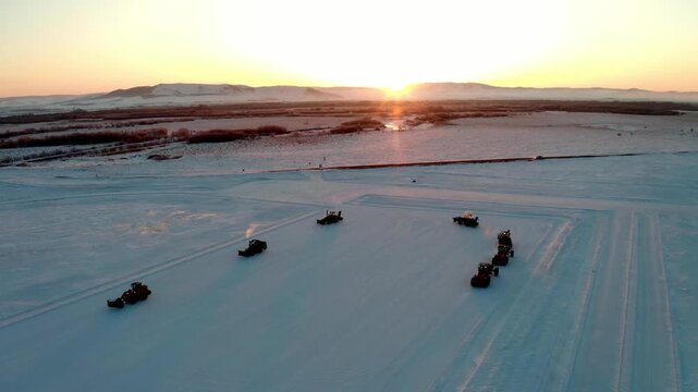 Snow Maintenance Convoy Curving Across a Plain at Sunset