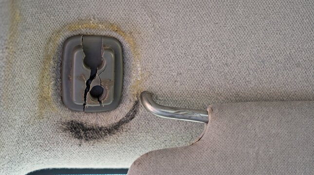 Damaged car interior sun visor clip and cracked plastic trim in a vehicle cabin.