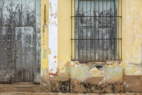 View of a weathered yellow colonial wall with a rustic wooden door and a window protected by iron bars in Remedios, Villa Clara, Cuba.