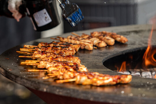 Preparing chicken meat skewers, grilled or roasted on a round griddle or a circular grill in a street food market